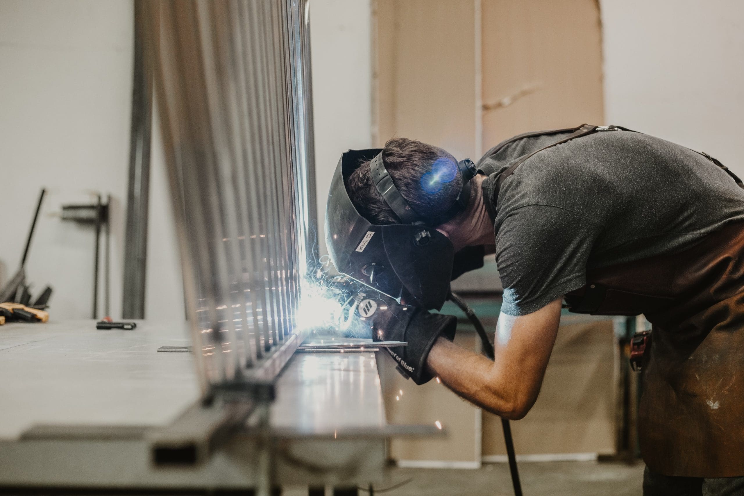 syd-mills-KAVGTm62cuw-unsplash Man wearing a mask welding metal parts in action, representing sheet metal fabrication services.